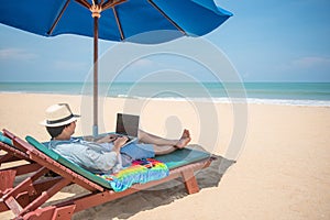 Young Asian man using laptop on beach bench