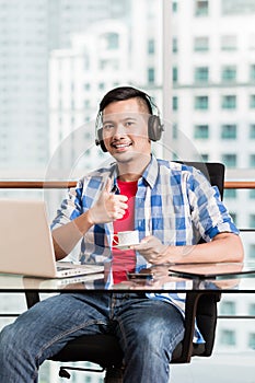 Young asian man in office having coffee giving thumbs up sign