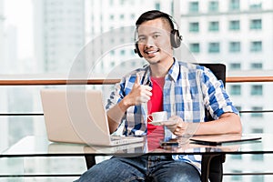Young asian man in office having coffee giving thumbs up sign