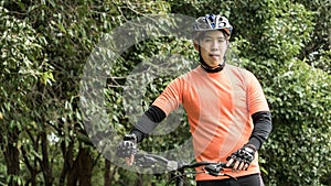 Young asian man in orange sportswear and mountain bike during recreation time in the park, Beautiful sunny day