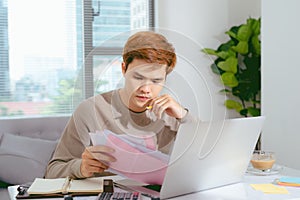 Young Asian man paying his bills at home in the living room