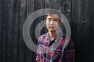 Confident young Asian man standing by a dark wall outside