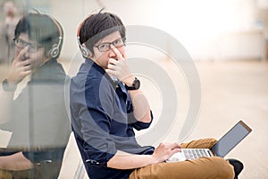 Young Asian man pushing glasses up on nose while using laptop