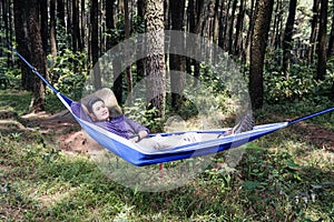 Young asian man relaxing on the hammock hanging among trees