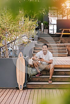 Young Asian man relaxing on steps outside reading text messages