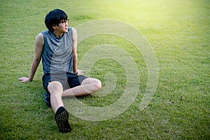 Young Asian man runner sitting on the grass after running