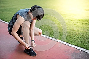 Young Asian man runner tying shoe laces on running trail