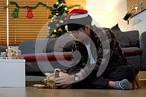 Young asian man in Santa hat sitting on floor and playing with his dog in living room