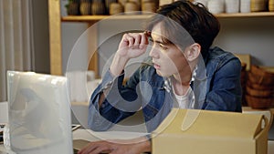 Young Asian man selling vases online stressed in front of laptop