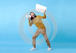 Young Asian man shouting into megaphone and holding speech bubble  on blue background