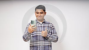 Young Asian man showing happy gesture while holding to his mobile phone and looking at camera
