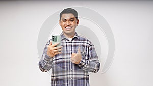 Young Asian man showing happy gesture while holding to his mobile phone and looking at camera