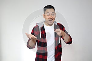 Young Asian man shows something on empty hand, smiling. Marketing advertising portrait with copy space