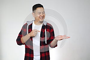 Young Asian man shows something on empty hand, smiling. Marketing advertising portrait with copy space