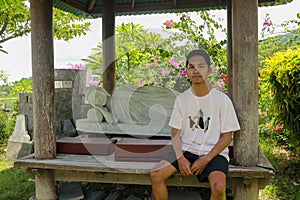 A young Asian man sits by a white Buddha statue lying in the Brahma Vihara Arama Temple. Statue of Sleeping Buddha at