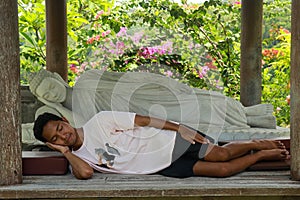 A young Asian man sits by a white Buddha statue lying in the Brahma Vihara Arama Temple. Statue of Sleeping Buddha at