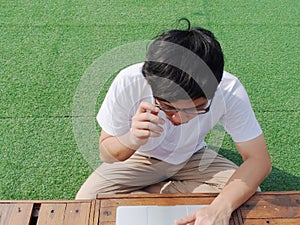Young Asian man sitting on grass and working on computer laptop.