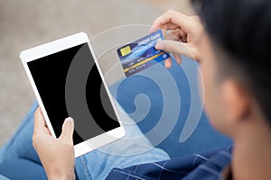 Young asian man smile holding credit card shopping online with tablet computer blank display screen buying and payment.