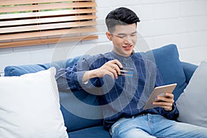Young asian man smiling holding credit card shopping online with tablet computer buying and payment.