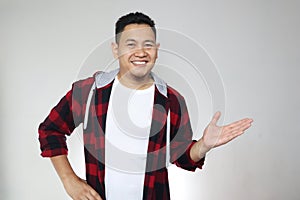 Young Asian man smiling, showing and pointing something on his side, against white wall with copy space