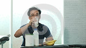 Young Asian man in sportswear sitting and drinking milk after weight training in Gym