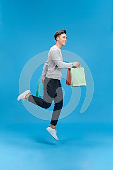 Young asian man super happy holding shopping bags, isolated on blue background