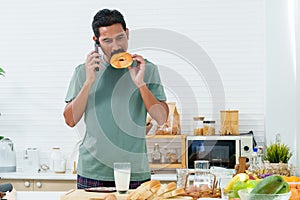 Young Asian man talking on phone in apartment in kitchen in morning after waking up, Wear comfortable pajamas, reaching out pick