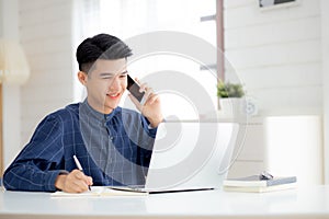 Young asian man talking phone and work from home with laptop computer.