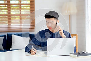 Young asian man talking phone and work from home with laptop computer.