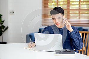 Young asian man talking phone and work from home with laptop computer.