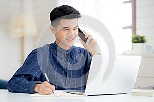 Young asian man talking phone and work from home with laptop computer.