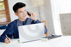 Young asian man talking phone and work from home with laptop computer.