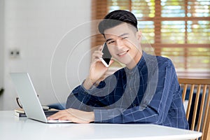 Young asian man talking phone and work from home with laptop computer.