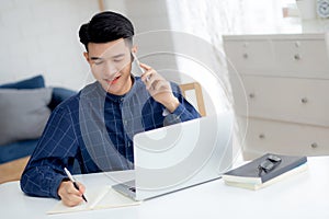 Young asian man talking phone and work from home with laptop computer.