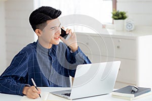Young asian man talking phone and work from home with laptop computer.