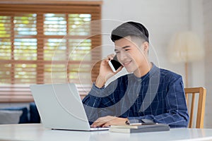 Young asian man talking phone and work from home with laptop computer, freelance using notebook to internet online.