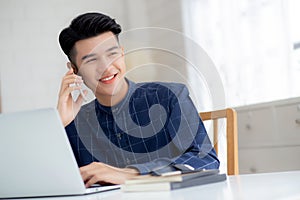 Young asian man talking phone and work from home with laptop computer, freelance using notebook to internet online.