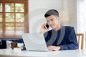 Young asian man talking phone and work from home with laptop computer, freelance using notebook to internet online.