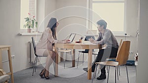 Young Asian man talking to confident businesswoman by the table. Multiethnic people talk in trendy modern office 4K.