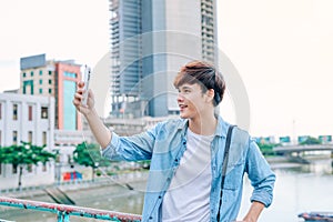 Young asian man tourist taking selfie photo using smartphone out