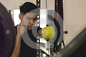 A young asian man training his punching reflexes and hand -eye coordination on a yellow double end bag. Boxing practice at the gym