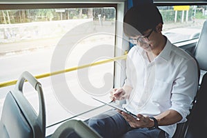 Young Asian man traveler sitting on a bus using tablet watch video or playing game while smile of happy, transport, tourism and