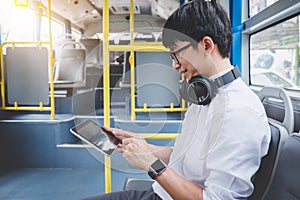Young Asian man traveler sitting on a bus using tablet watch video or playing game while smile of happy, transport, tourism and r