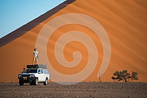 Young Asian man traveler standing on camper car near orange sand