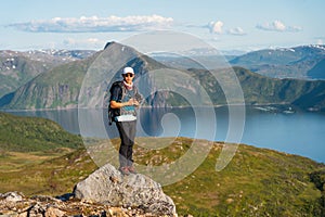 Young Asian man traveller with backpack and camera standing on rock at Senja island in summer season, Norway, Scandinavia