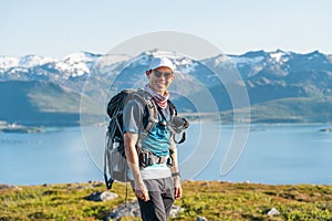 Young Asian man traveller with backpack standing on rock at Senja island in summer season. A man with smiley face enjoying outdoor