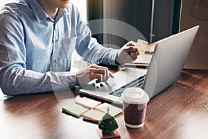 Young asian man typing laptop keyboard and holding credit card at home with online shopping or internet banking concept