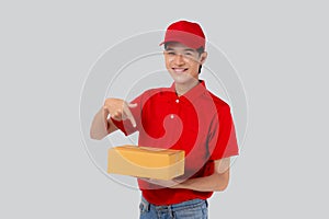 Young asian man in uniform red and cap carrying box and presenting with excited isolated white background.