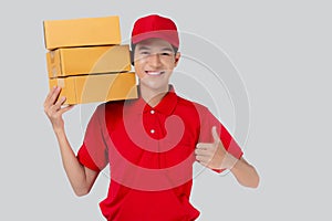 Young asian man in uniform red and cap standing carrying box stack and thumbs up isolated white background.