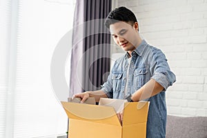 Young Asian man unpacking received parcel. He is satisfied with Internet order shopping online, delivery service concept